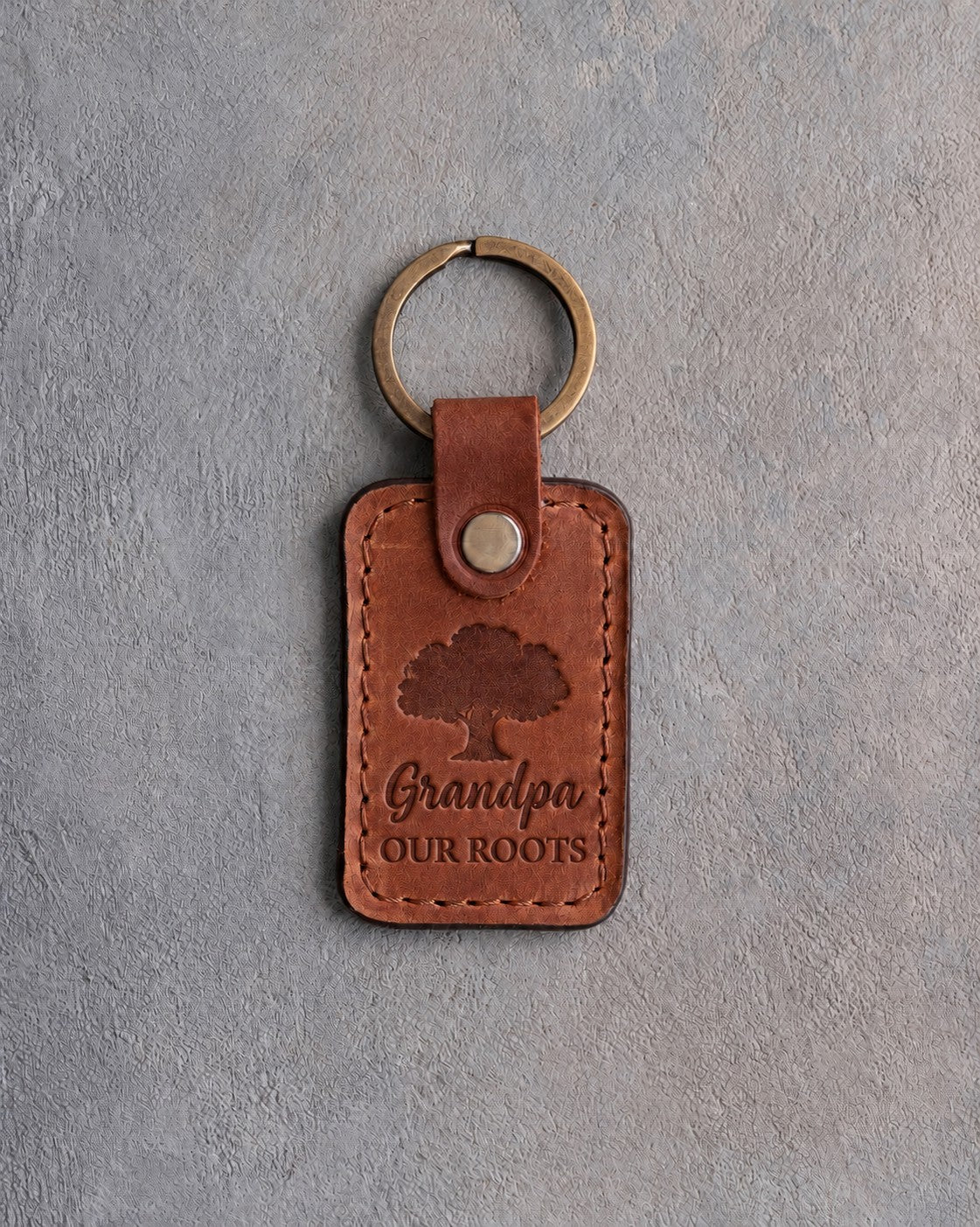 Arizona tan leather keychain debossed with a solid oak tree above Grandpa and OUR ROOTS, on gray concrete
