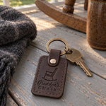 Dark brown Grandpa's CHAIR keychain on the arm of a wooden rocking chair on a porch