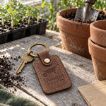 Reddish brown Grandpa's Garden keychain on the handle of an old wheelbarrow beside a vegetable bed