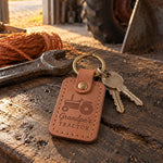 Caramel Grandpa's Tractor keychain on an oil-dark workbench in a farm shop beside a wrench and baler twine, sun coming through the open bay door