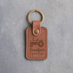 Caramel leather keychain debossed with an open-station tractor above the words Grandpa's TRACTOR, on gray concrete