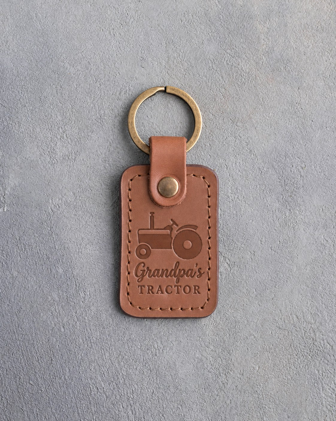 Caramel leather keychain debossed with an open-station tractor above the words Grandpa's TRACTOR, on gray concrete