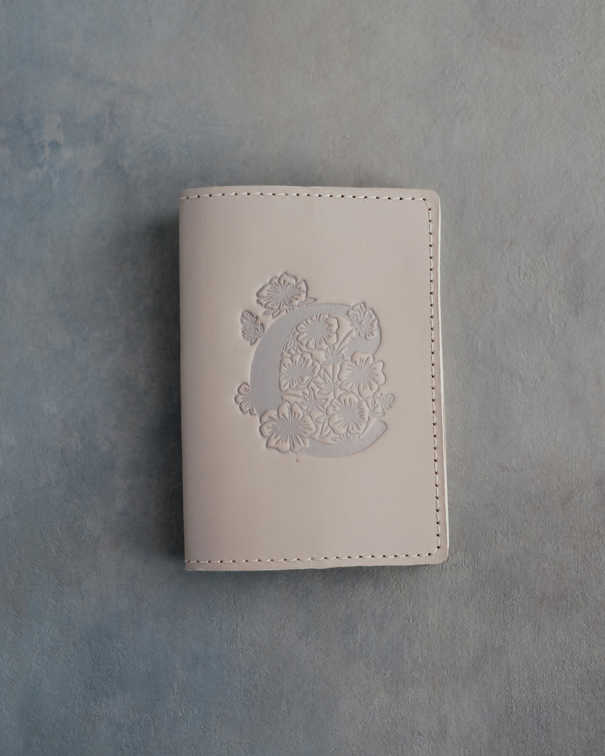 Gray Sand leather passport cover with a large floral initial C pressed into the front