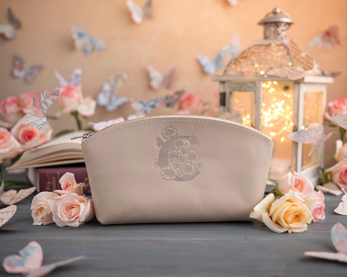 Cream leather makeup pouch with a soft floral monogram, beside a glowing lantern