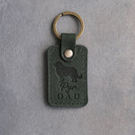 Forest green leather keychain debossed with a Great Pyrenees silhouette and Pyr DAD on gray concrete