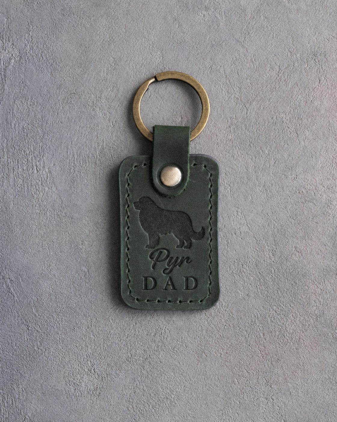 Forest green leather keychain debossed with a Great Pyrenees silhouette and Pyr DAD on gray concrete