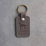 Country gray leather keychain debossed with a golden retriever silhouette and the words Greets WITH A SHOE, on gray concrete