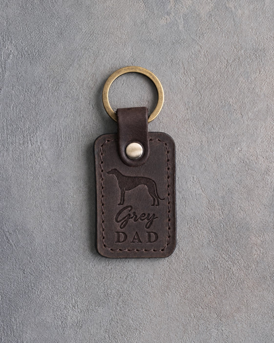 Dark espresso leather keychain debossed with a greyhound silhouette and Grey DAD, on gray concrete