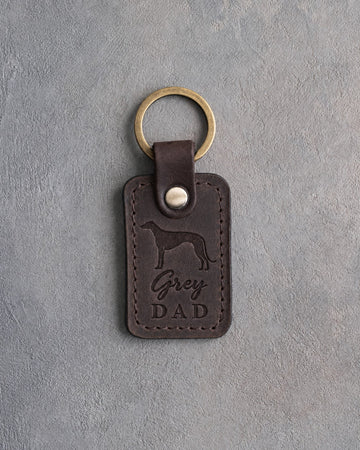 Dark espresso leather keychain debossed with a greyhound silhouette and Grey DAD, on gray concrete
