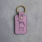Lilac leather keychain with a debossed greyhound and the words Grey MOM on gray concrete