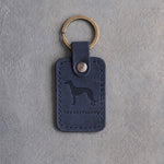 Blueberry navy leather keychain debossed with a greyhound above THE GREYHOUND, on gray concrete