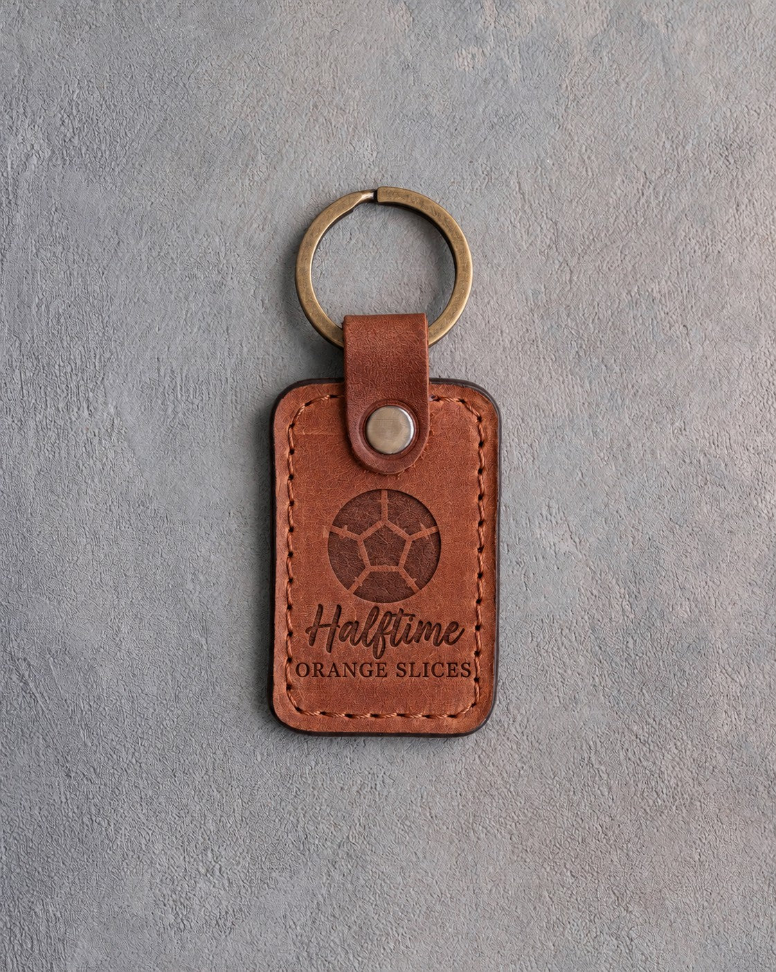 Arizona orange tan leather keychain debossed with a soccer ball and the words Halftime ORANGE SLICES, on gray plaster