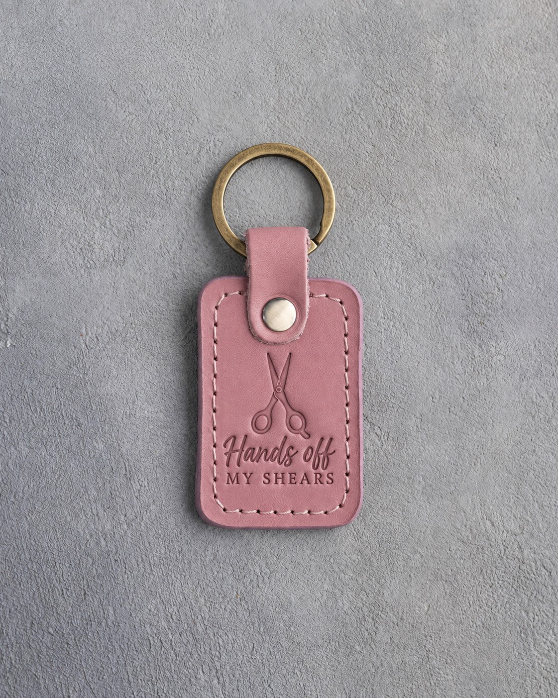 Parisian Blossom pink leather keychain debossed with a pair of open grooming shears and the words Hands off MY SHEARS, on gray concrete