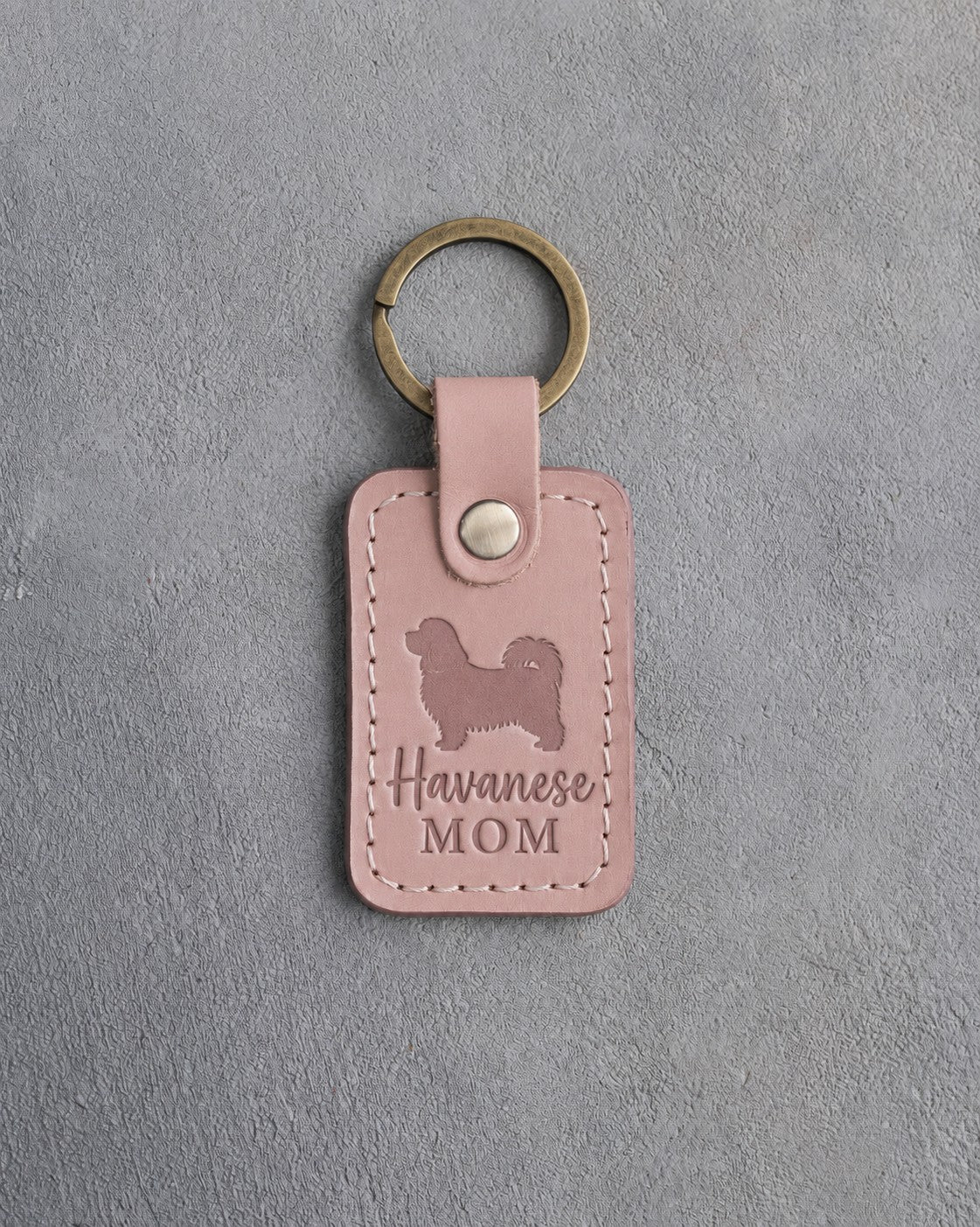 Blush pink leather keychain with a debossed Havanese and the words Havanese MOM on gray concrete