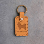 Indian Summer tan leather keychain debossed with a Havanese above THE HAVANESE, on gray concrete