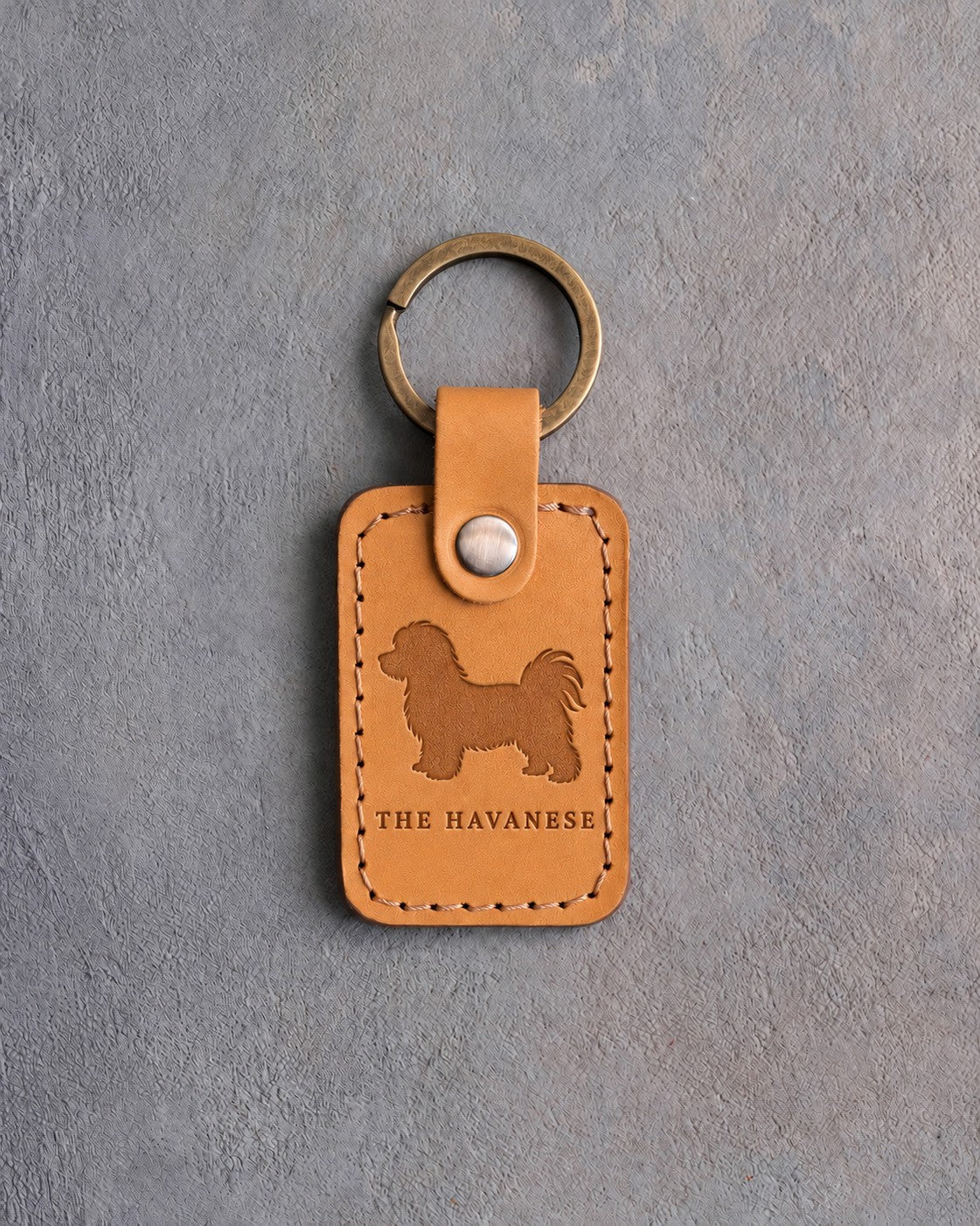 Indian Summer tan leather keychain debossed with a Havanese above THE HAVANESE, on gray concrete