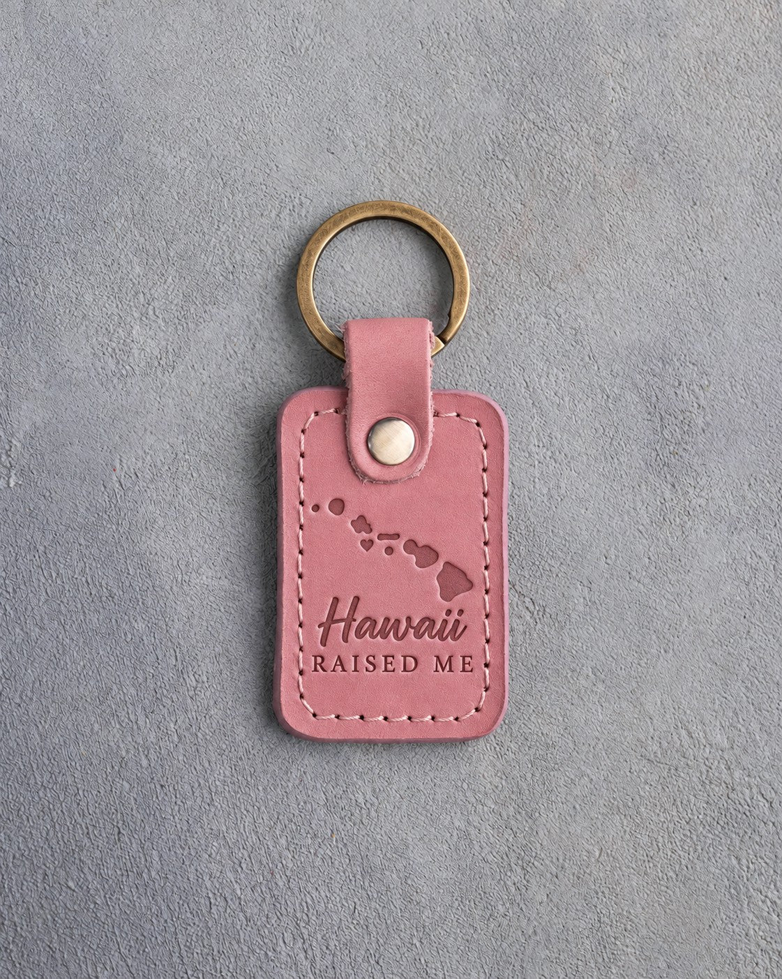 Parisian Blossom pink leather keychain debossed with the Hawaiian island chain and a heart off Oahu above Hawaii and RAISED ME, on gray concrete