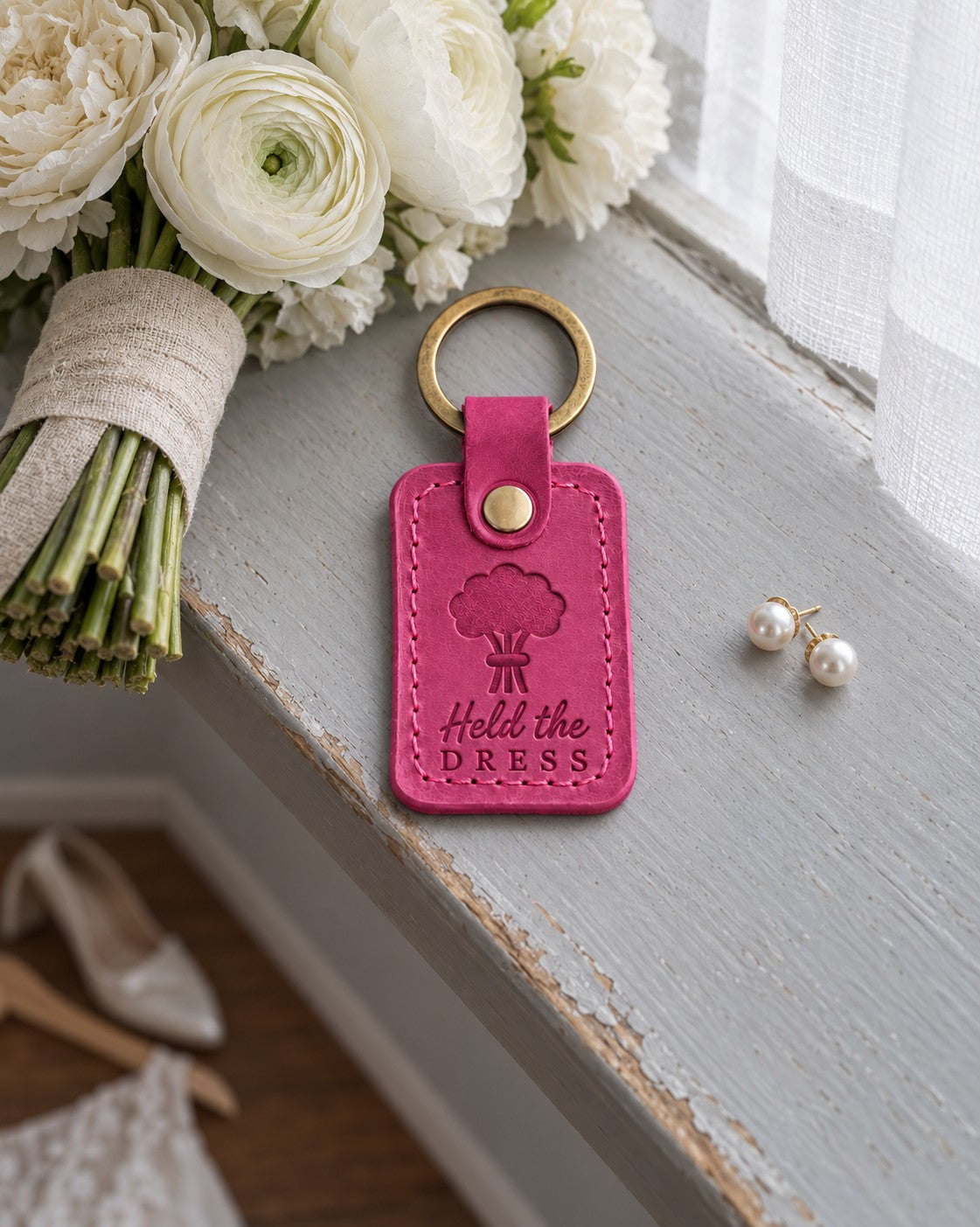 Held the DRESS keychain in fuchsia leather on a gray windowsill with a satin shoe soft in the background