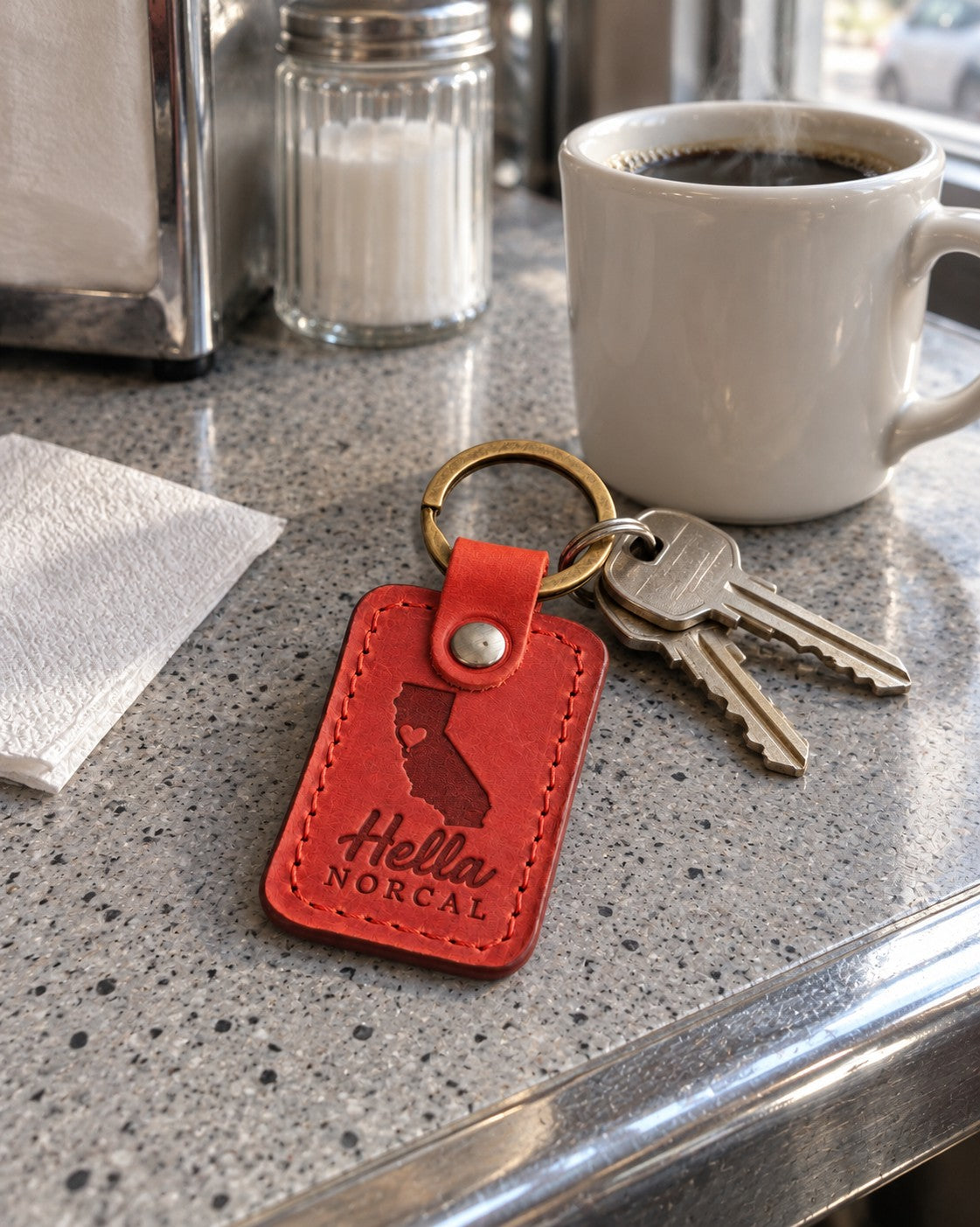 Red Hella NorCal keychain on car keys resting on a foggy hillside overlook above the bay