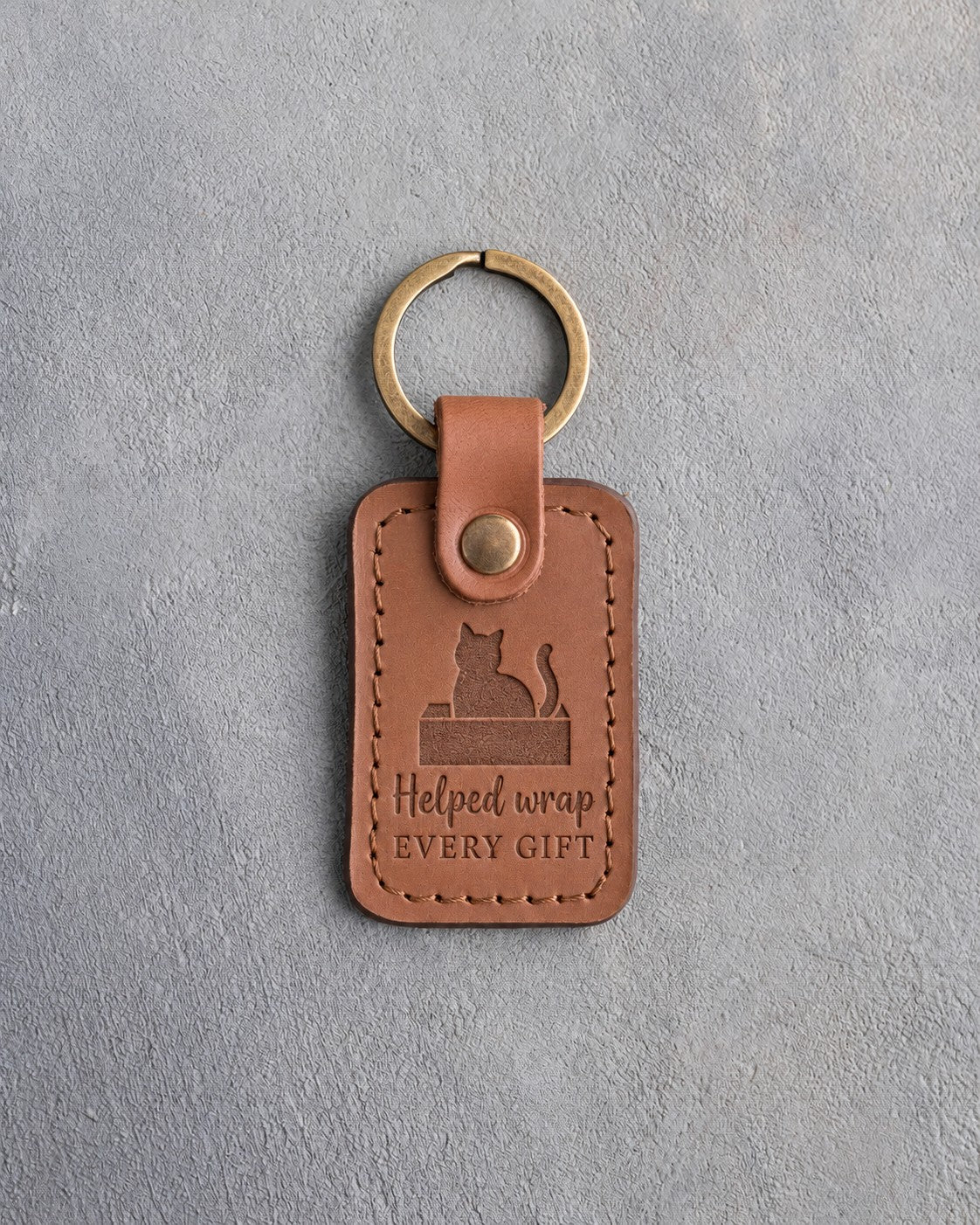 Caramel leather keychain debossed with a cat sitting in an open box above the words Helped wrap EVERY GIFT