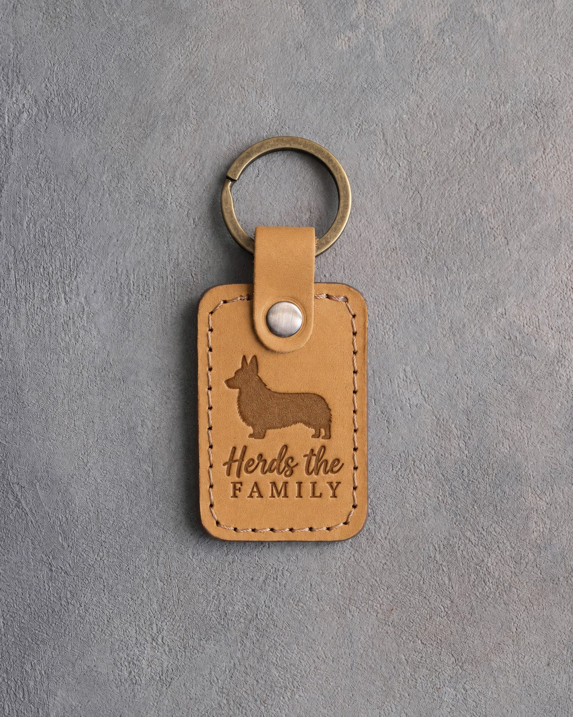 Indian Summer tan leather keychain debossed with a corgi silhouette and the words Herds the FAMILY, on gray concrete