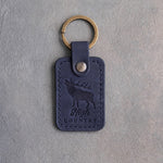 Blueberry navy leather keychain debossed with a bugling bull elk above the words High COUNTRY, on gray plaster