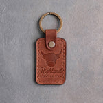 Arizona tan leather keychain debossed with a shaggy highland cow above the words Highland and COW LOVER, on gray concrete