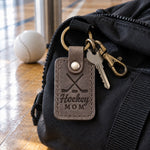 Gray Hockey Mom keychain on car keys resting on a rink bench beside a travel coffee mug
