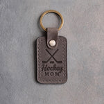 Country gray leather keychain debossed with crossed hockey sticks and a puck above the words Hockey MOM, on gray plaster