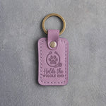 Lilac leather keychain debossed with a paw print circled by a stethoscope and the words Holds the WIGGLY END, on gray concrete