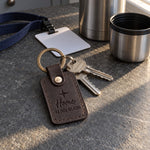 Dark brown Home coordinates keychain on house keys resting on a lake cabin porch rail at sunset