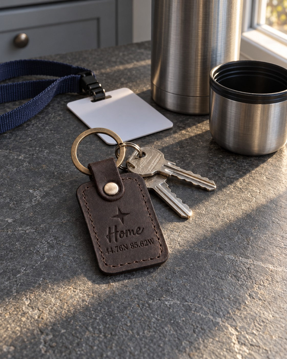 Dark brown Home coordinates keychain on house keys resting on a lake cabin porch rail at sunset