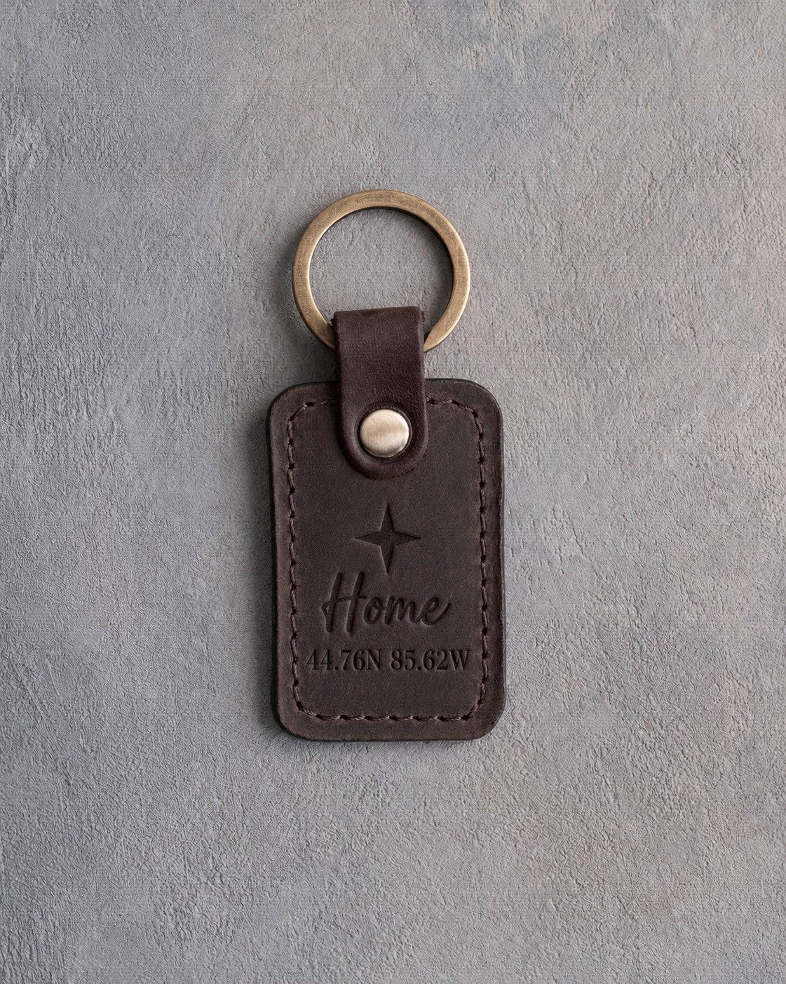 Dark espresso leather keychain debossed with a four-point star above Home and 44.76N 85.62W, on gray concrete