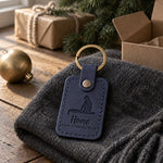 Navy Home for Christmas keychain on a windowsill beside a candle on a winter evening