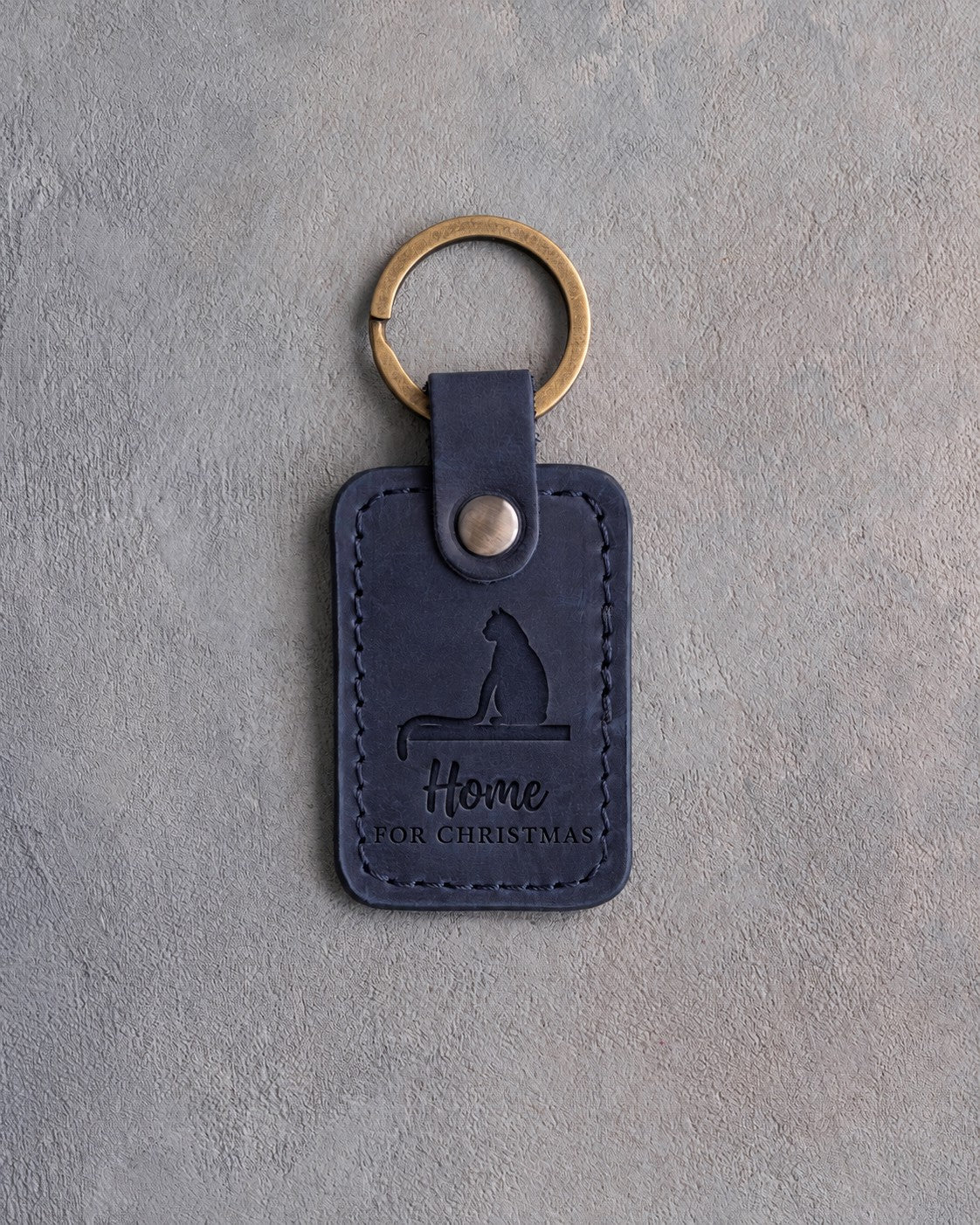 Blueberry navy leather keychain debossed with a cat on a windowsill above the words Home FOR CHRISTMAS