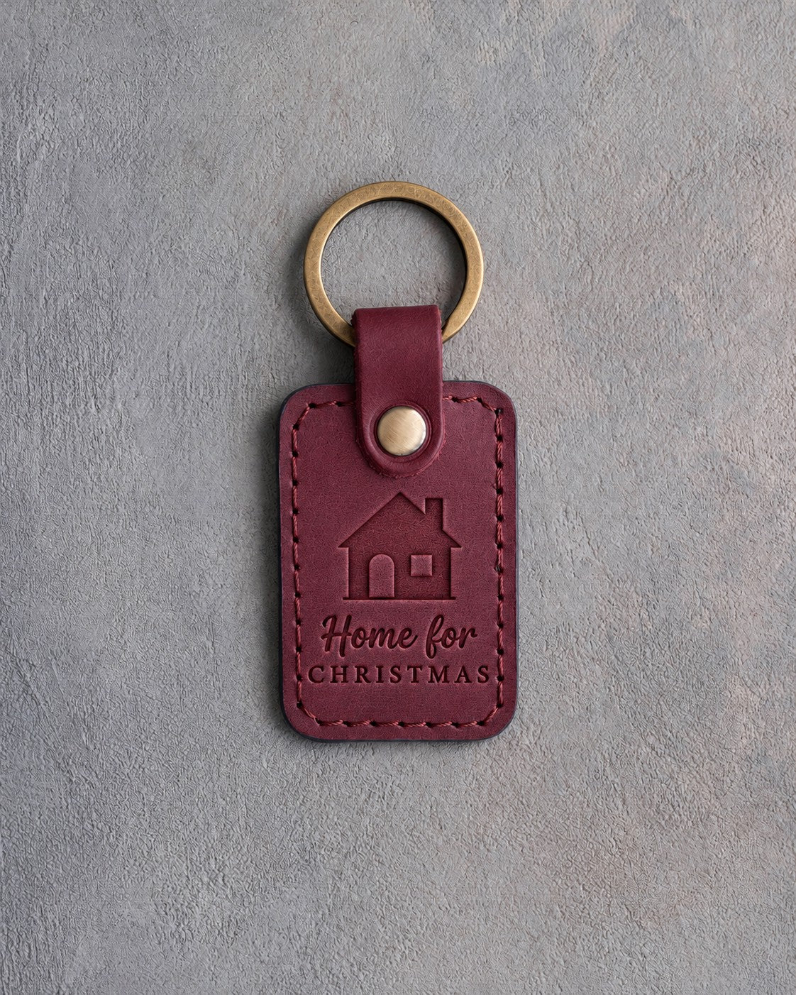 Sangria red leather keychain debossed with a gable-front house above Home for and CHRISTMAS, on gray concrete