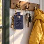 Navy Home is WHERE MOM IS keychain on house keys by a front door with the porch light on at dusk