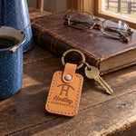Hadley HOMESTEAD keychain in Indian Summer leather on a dark oak ranch kitchen table beside a closed leather ledger and reading glasses