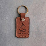 Arizona tan leather keychain debossed with a Tumbling T ranch brand above the name Tate and HORSES, on gray plaster