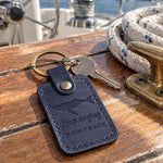 Blueberry Keep singing HUMPBACK keychain in full-grain leather on the worn teak cockpit table of a sailboat beside a coiled white dock line