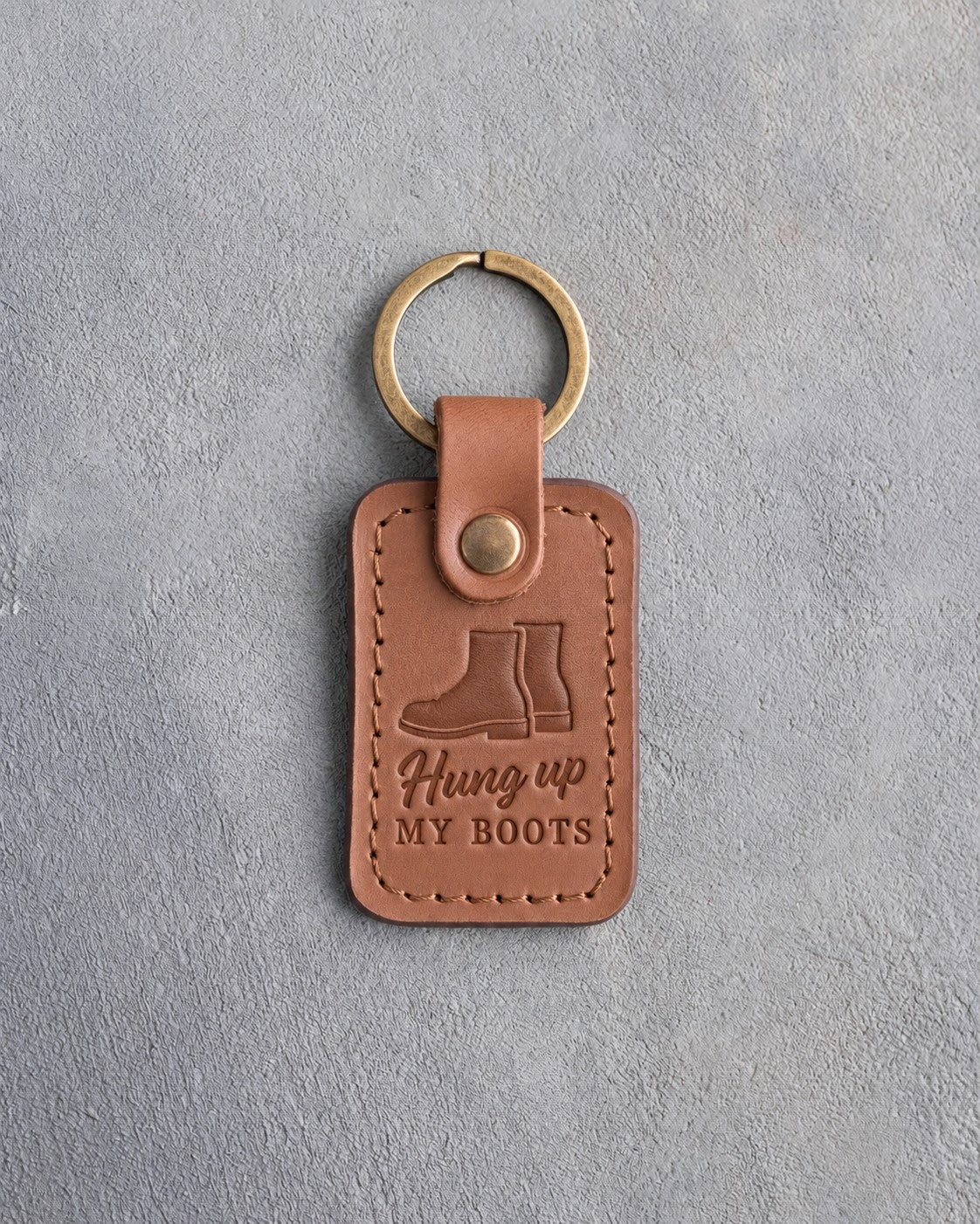 Caramel leather keychain debossed with a pair of service boots above the words Hung up MY BOOTS, on gray concrete