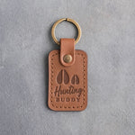 Caramel leather keychain debossed with a large deer track and a small fawn track above the words Hunting BUDDY, on gray plaster