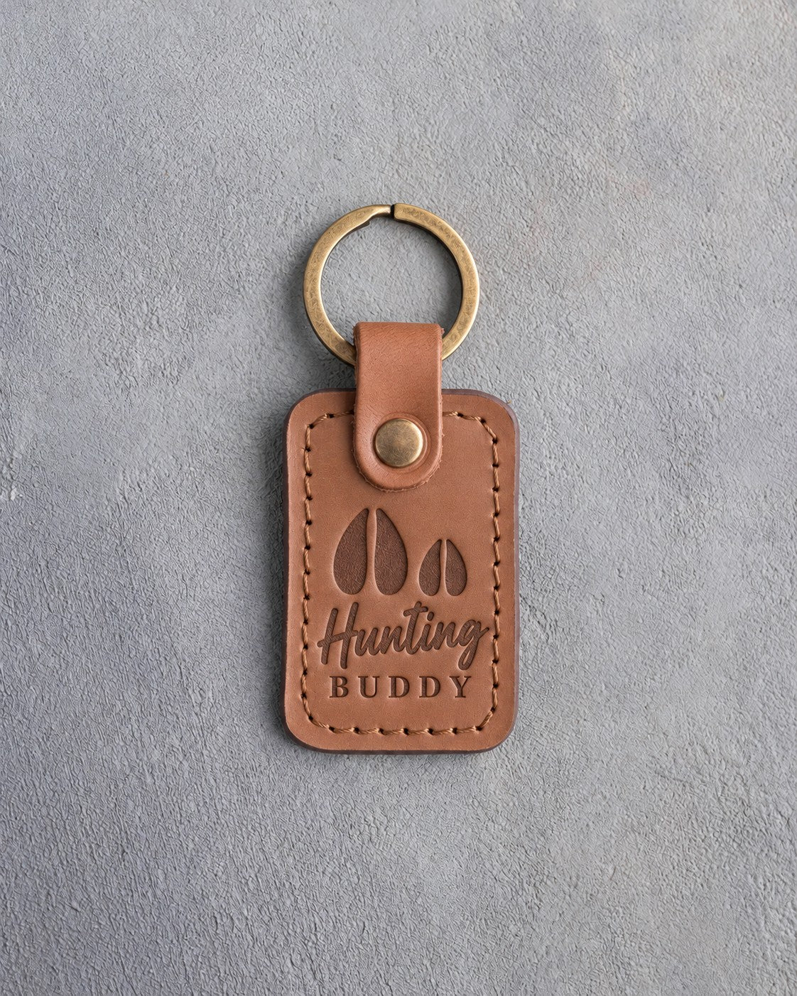 Caramel leather keychain debossed with a large deer track and a small fawn track above the words Hunting BUDDY, on gray plaster