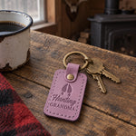 Lilac Hunting Grandma keychain on a key ring beside a blaze orange knit hat on a farmhouse porch bench