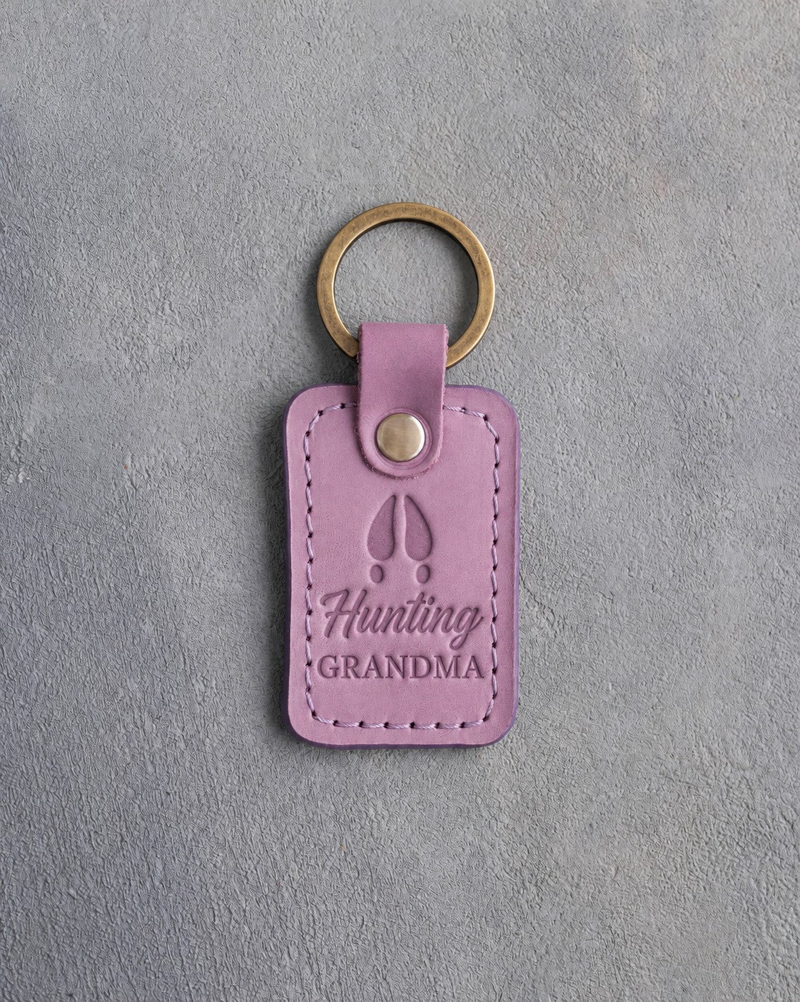 Lilac leather keychain debossed with a whitetail deer track above the words Hunting GRANDMA, on gray plaster