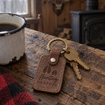 Hunting Grandpa keychain in brown leather on an older man's key ring beside a pair of binoculars on a flannel shirt