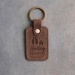 Sicilian brown leather keychain debossed with a deer track and a fawn track above the words Hunting GRANDPA, on gray plaster