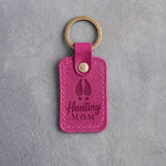Fuchsia pink leather keychain debossed with a whitetail deer track and the words Hunting MOM, on gray plaster