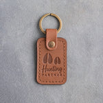 Caramel leather keychain debossed with a large deer track and a small deer track above the words Hunting PARTNER, on gray plaster