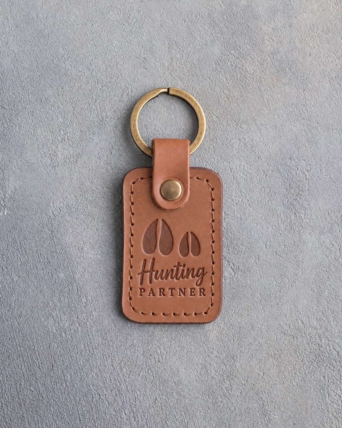 Caramel leather keychain debossed with a large deer track and a small deer track above the words Hunting PARTNER, on gray plaster